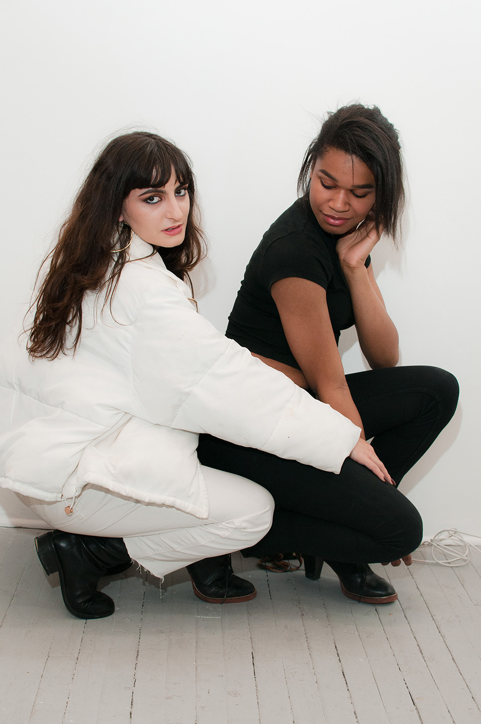 Two female figues looking coyly at the camera crouching next to each other